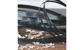 Metal bandsaw blades coiled together with wood shavings scattered on a surface, showcasing cutting tools and materials.