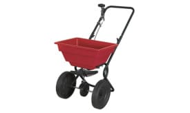 Red garden spreader with large wheels for easy movement, ideal for spreading seeds, fertiliser, or other materials in gardens.